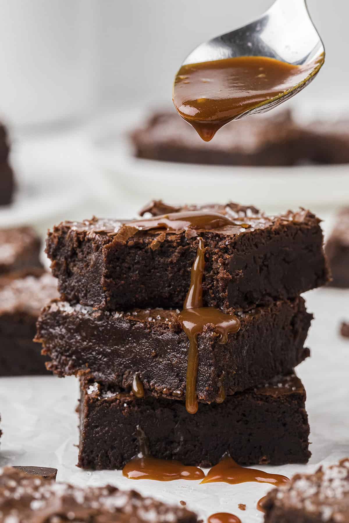 Stack of fudgy brownies with salted caramel being drizzled over the top.
