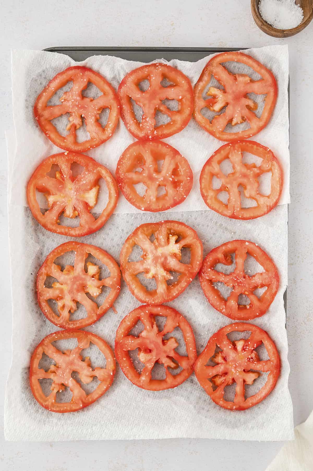 Sliced tomatoes on paper towel lined baking sheet.