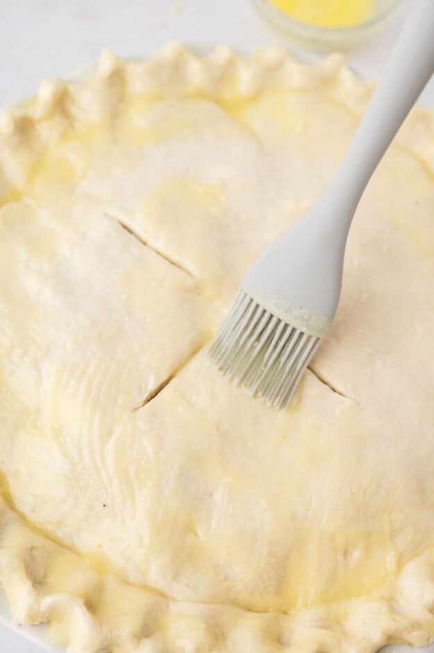 Pie crust being brushed with melted butter.