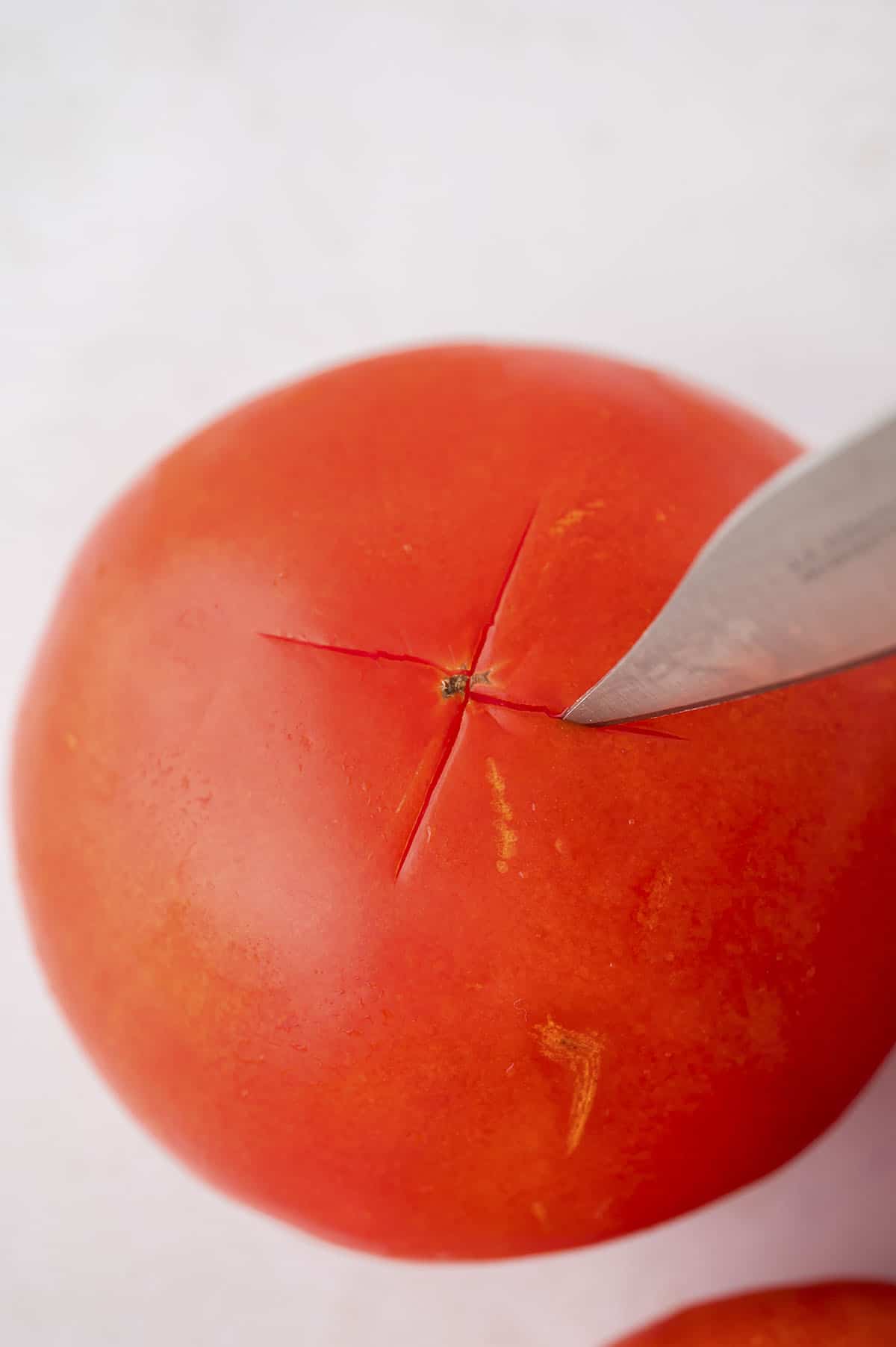 Knife cutting an 'x' into a tomato.