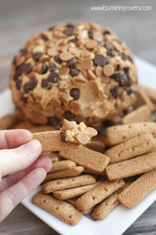 A person holding up a cookie with a scoop of a peanut butter cheese ball on it.