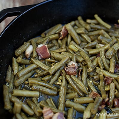 A closeup of green beans and bacon cooking in a cast iron skillet