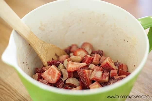 A wooden spoon in a bowl of cut strawberries 