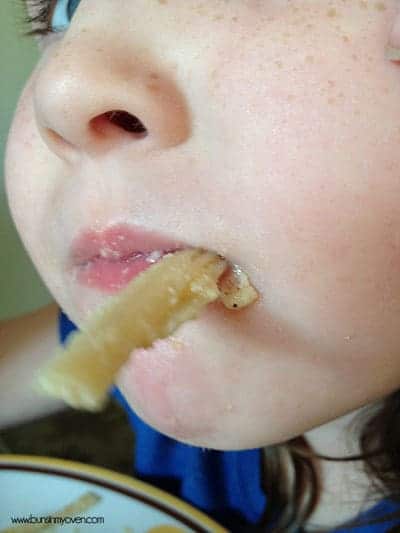 A closeup of a kid with a noodle in their mouth 