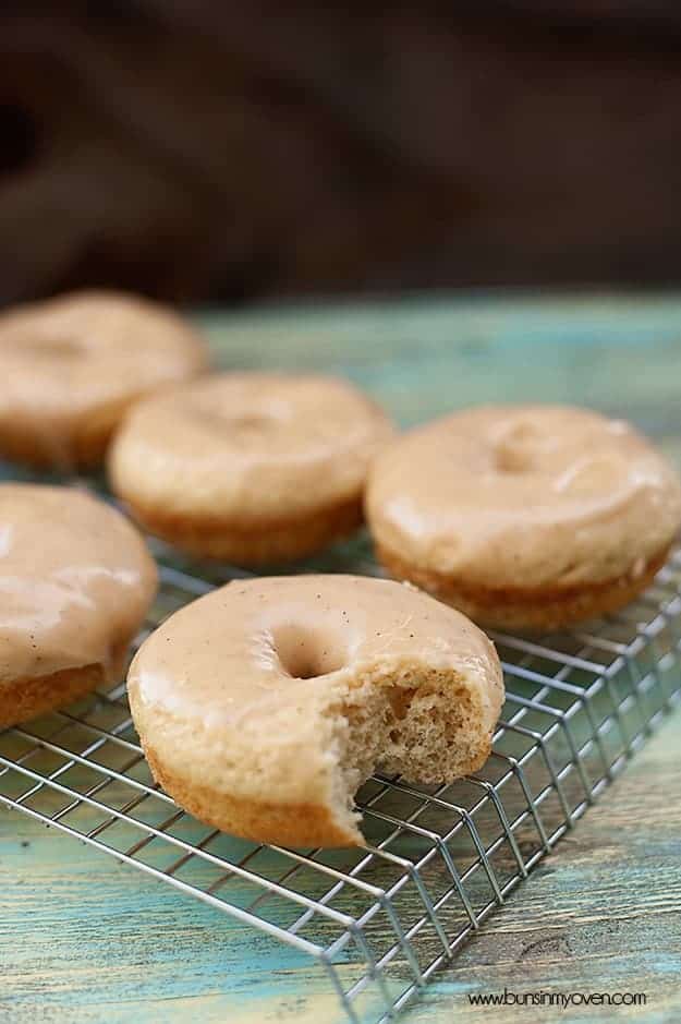 Six brown butter glazed donuts on a cooling rack, and the front one has a bite taken out of it.