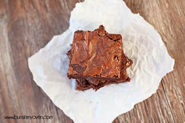 An overhead view of three brownies stacked up on a white napkin.