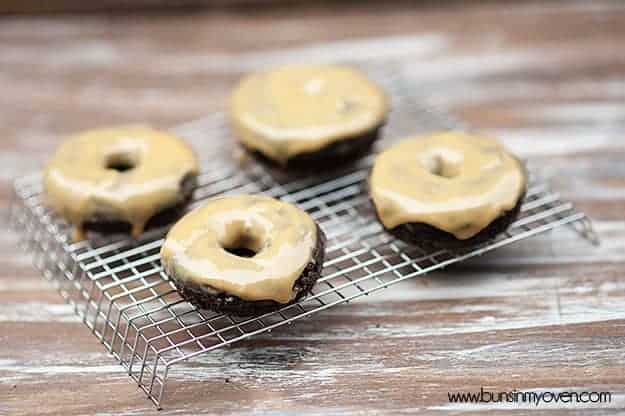 Four donuts with peanut butter icing on a cooling wire rack.