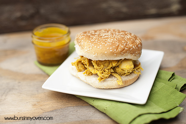 A sandwich sitting on top of a wooden table next to a jar of yellow barbecue sauce.