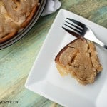 A top down view of a slice of a cinnamon roll with browned butter icing on a white plate next to a fork.