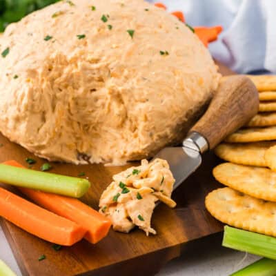 Buffalo chicken cheese ball surrounded by crackers and veggies on wooden board.