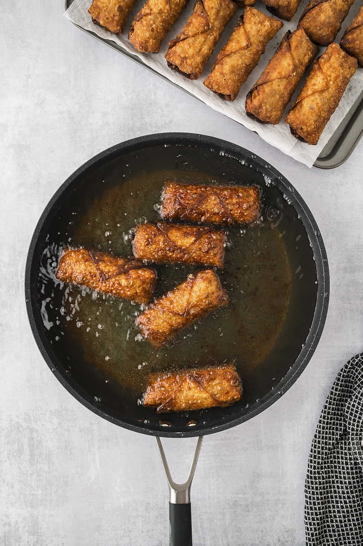 Egg rolls frying in skillet full of oil.