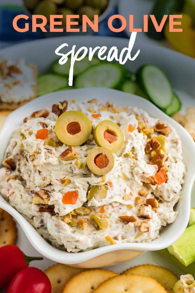 Olive spread in bowl surrounded by crackers and vefetables.