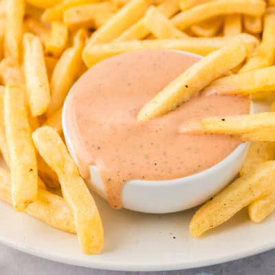 A pile of french fries next to a dish of fry sauce.