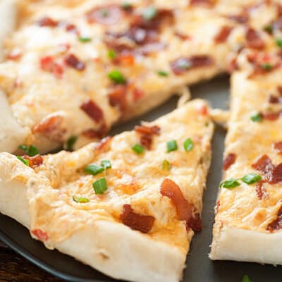 A close up of a slice of bacon cheese pizza cut from the rest of the pizza.
