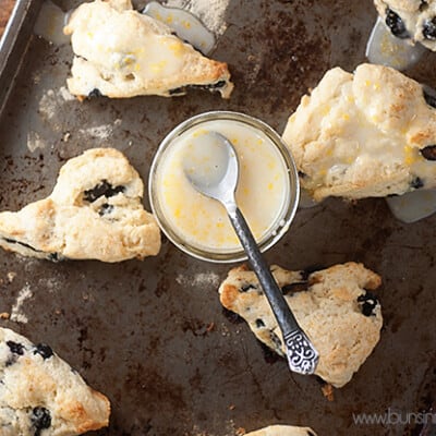 Overhead view of scones and a jar of lemon glaze on a baking sheet.