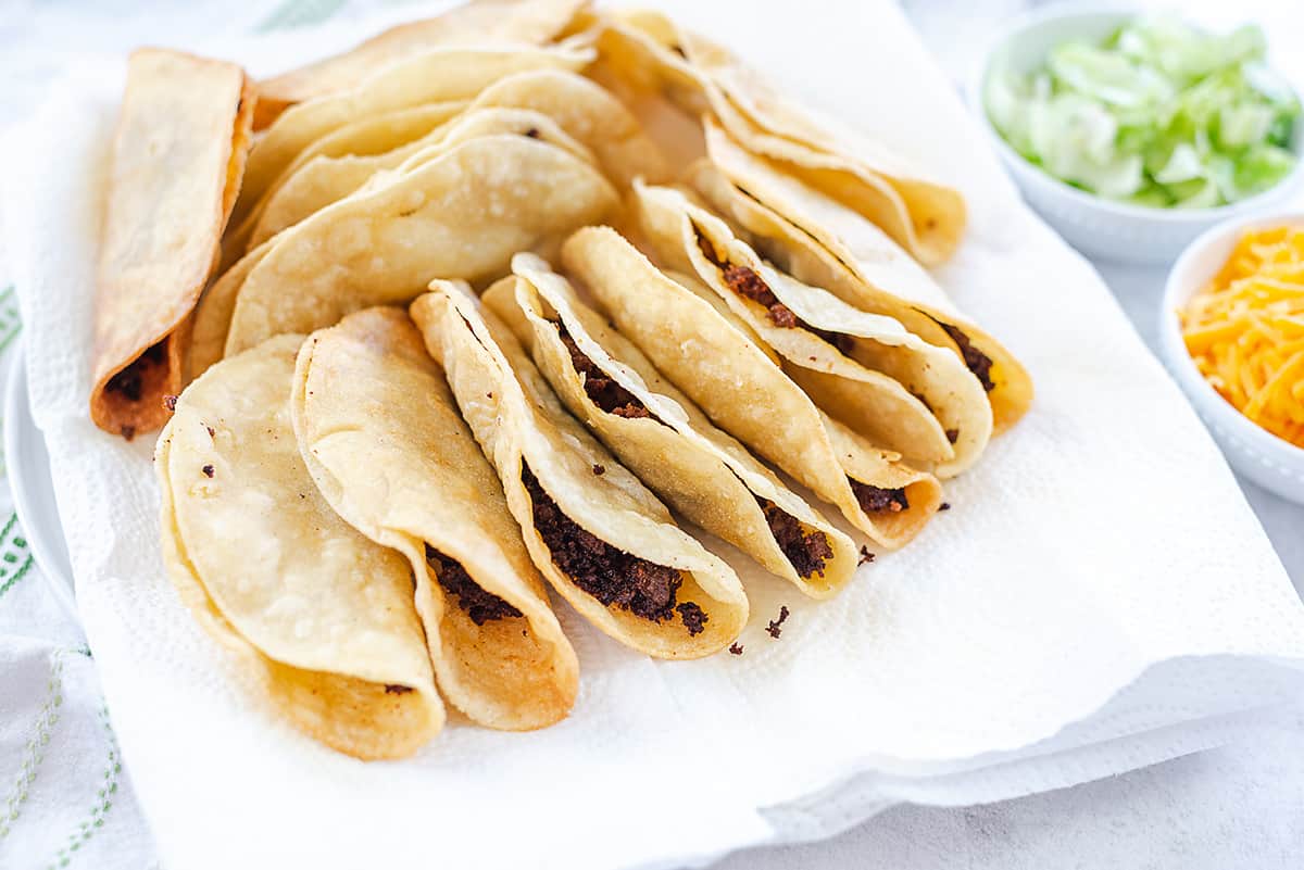 fried tacos draining on paper towel lined plate.