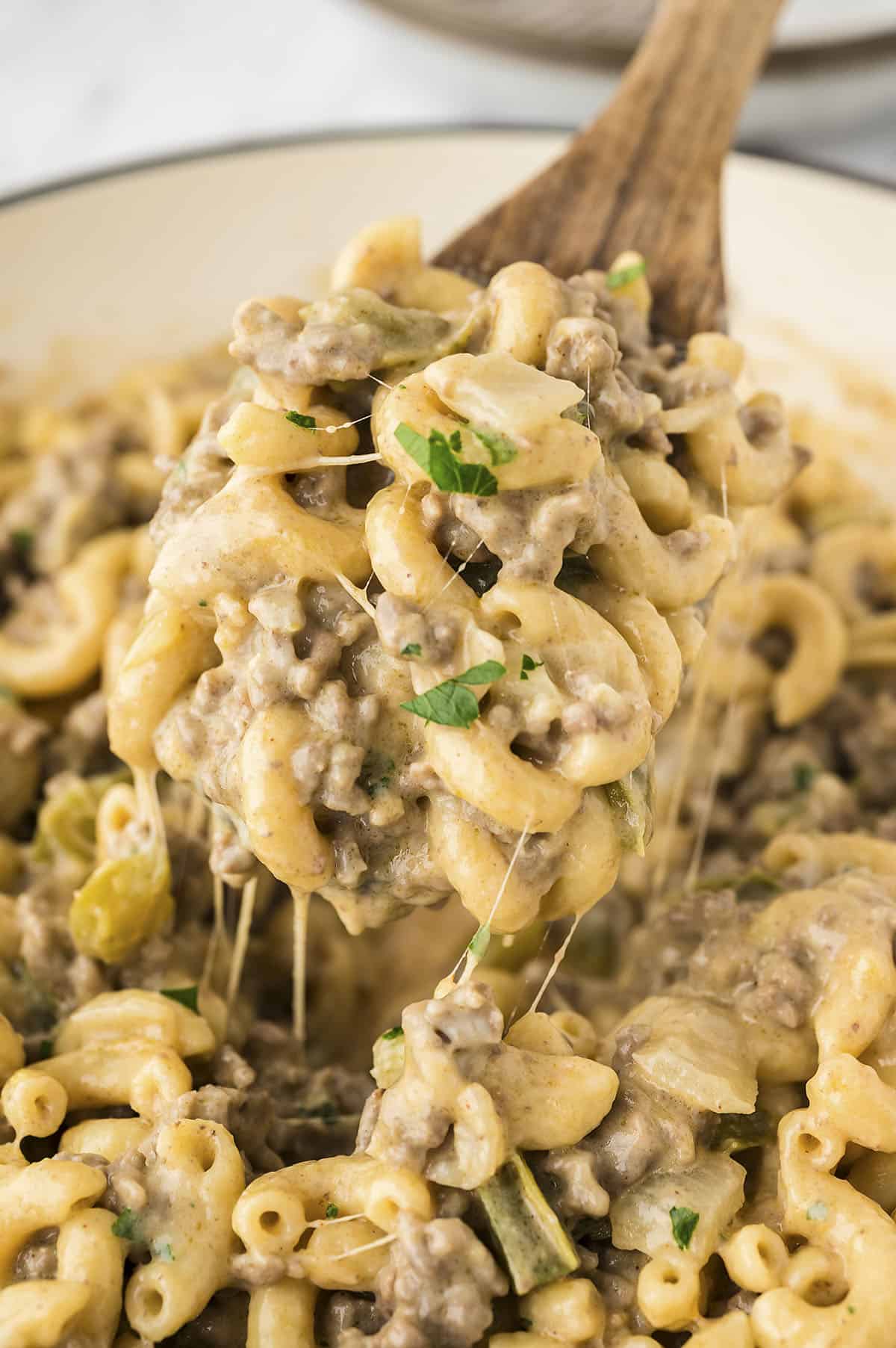 Philly cheesesteak pasta on wooden spoon in pan.