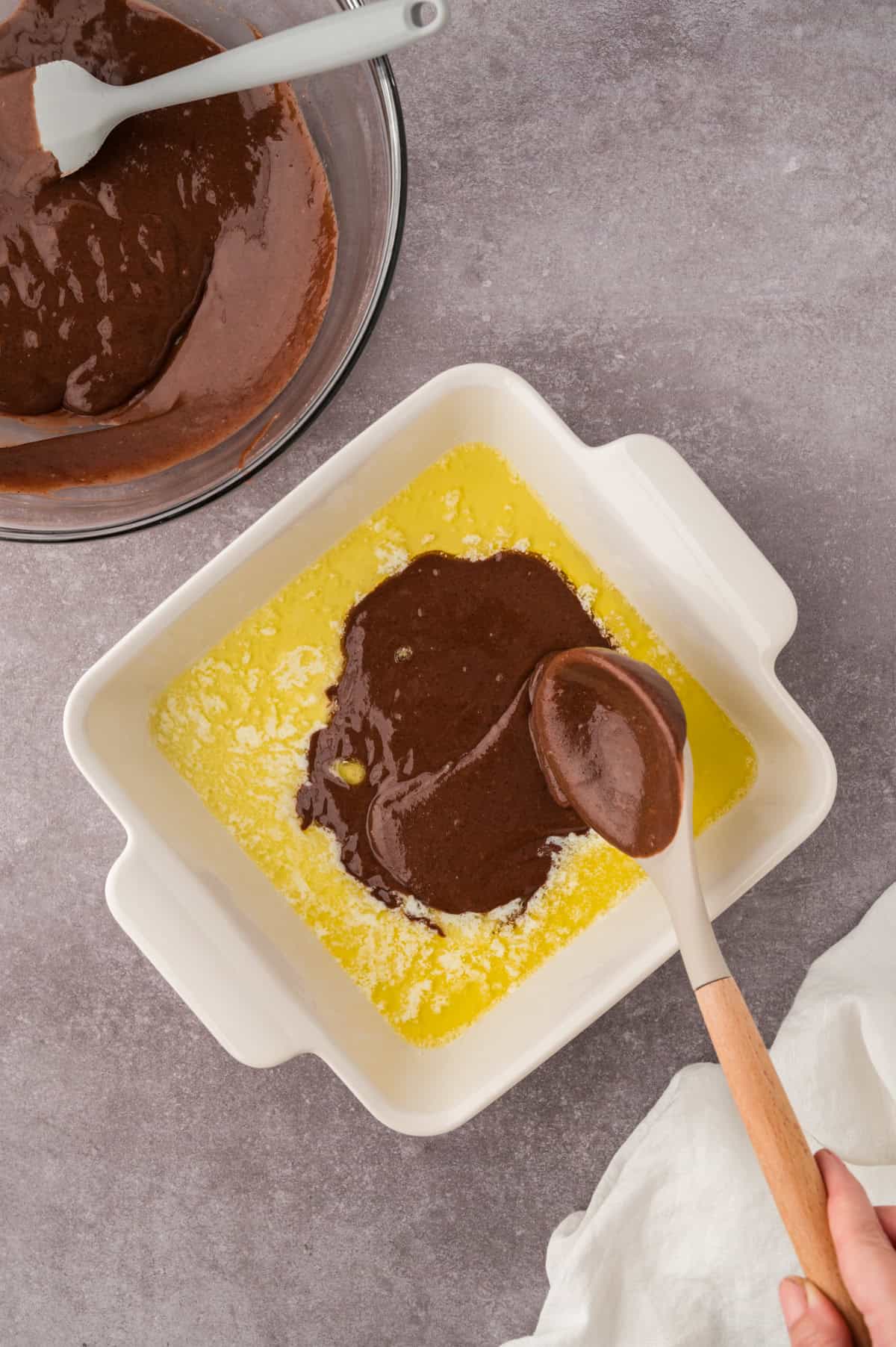 Chocolate cobbler filling being drizzled over melted butter.