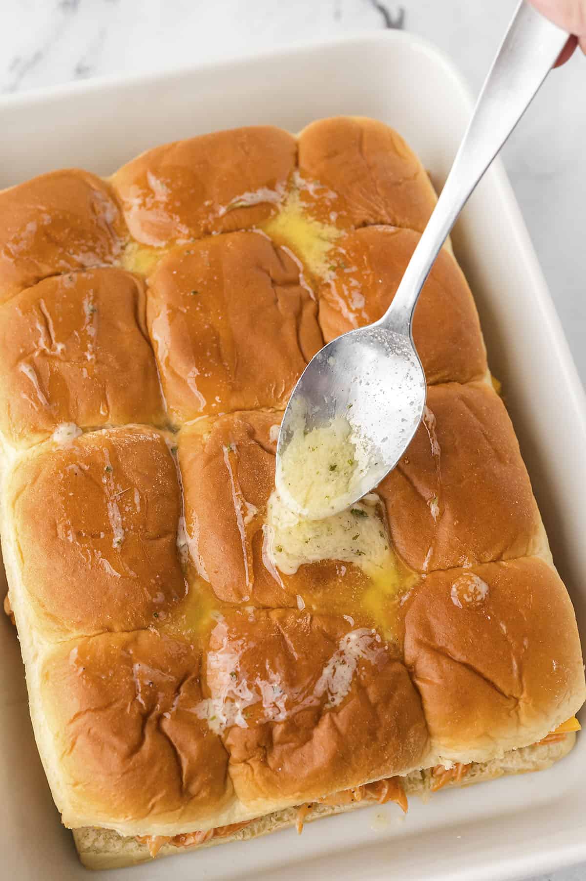 Ranch butter being drizzled over sliders.