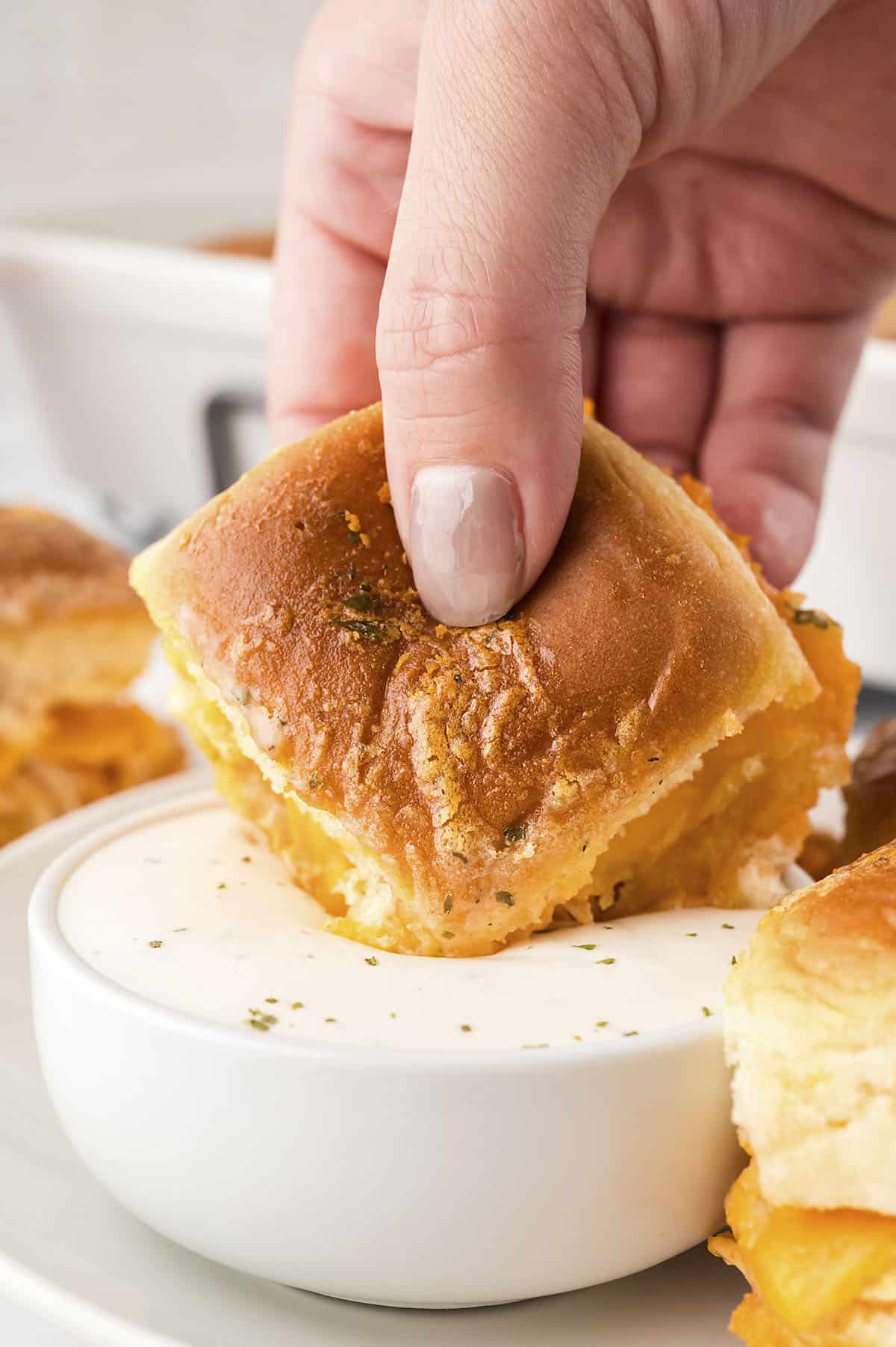 Hand dipping a buffalo chicken slider into ranch dressing.