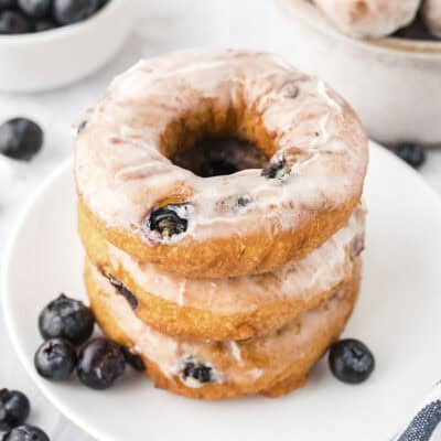 Stack of blueberry donuts on small white plate.