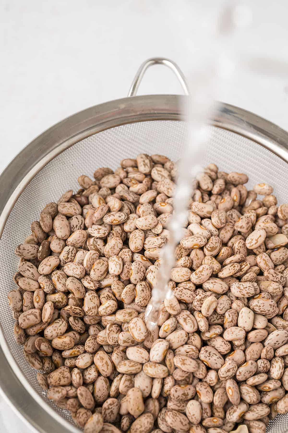 Beans in a colander with water running over them.
