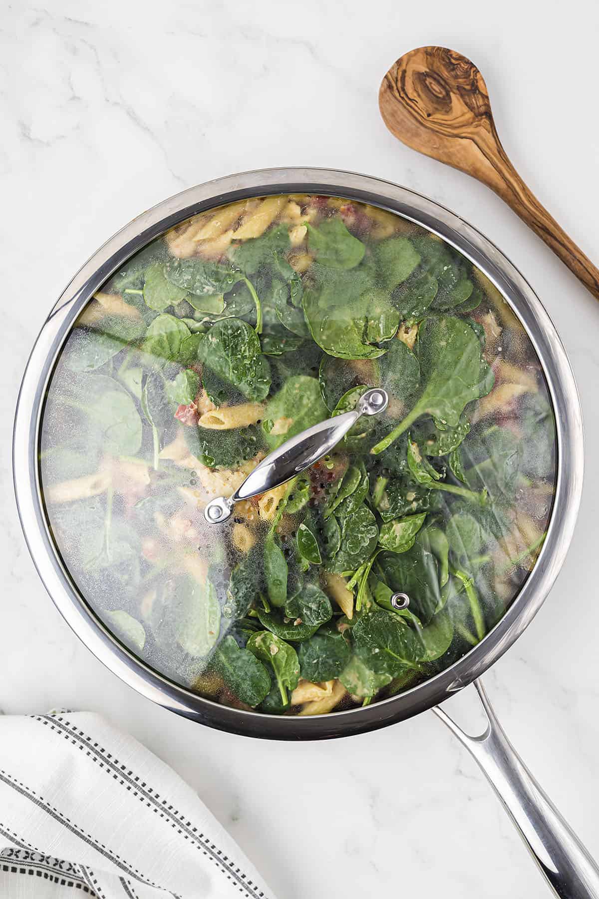 Spinach in skillet with lid on.