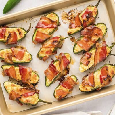 Bacon wrapped jalapeno poppers on baking sheet.