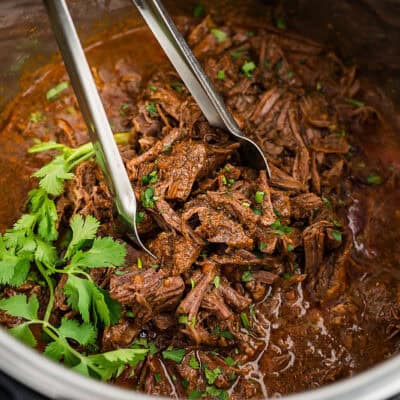 Barbacoa in Instant Pot with tongs.