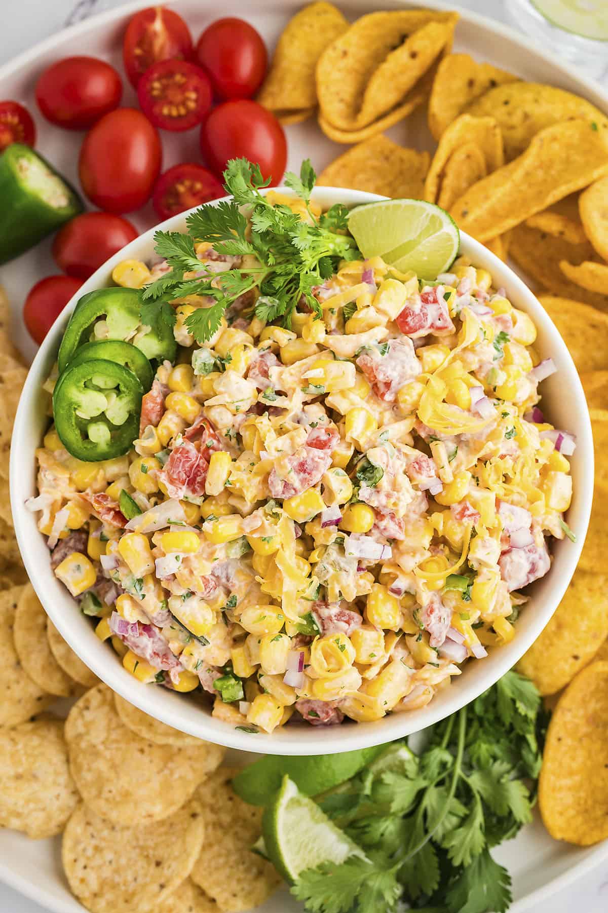 Cold corn dip in bowl surrounded by chips and vegetables.