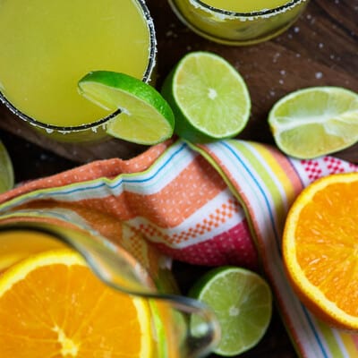 Un vaso de margarita junto a un racimo de naranjas cortadas.