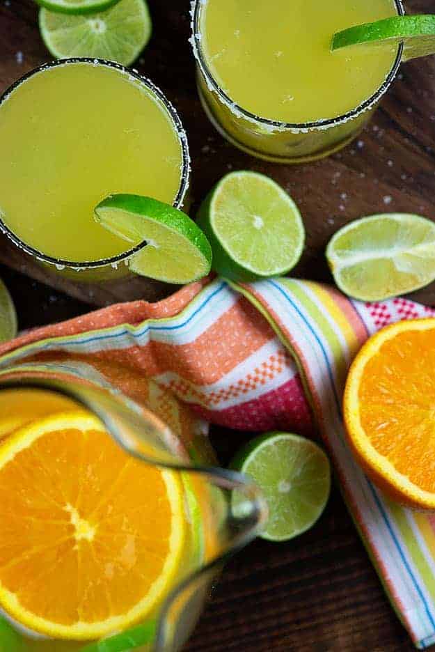 Un vaso de margarita junto a un puñado de naranjas cortadas.