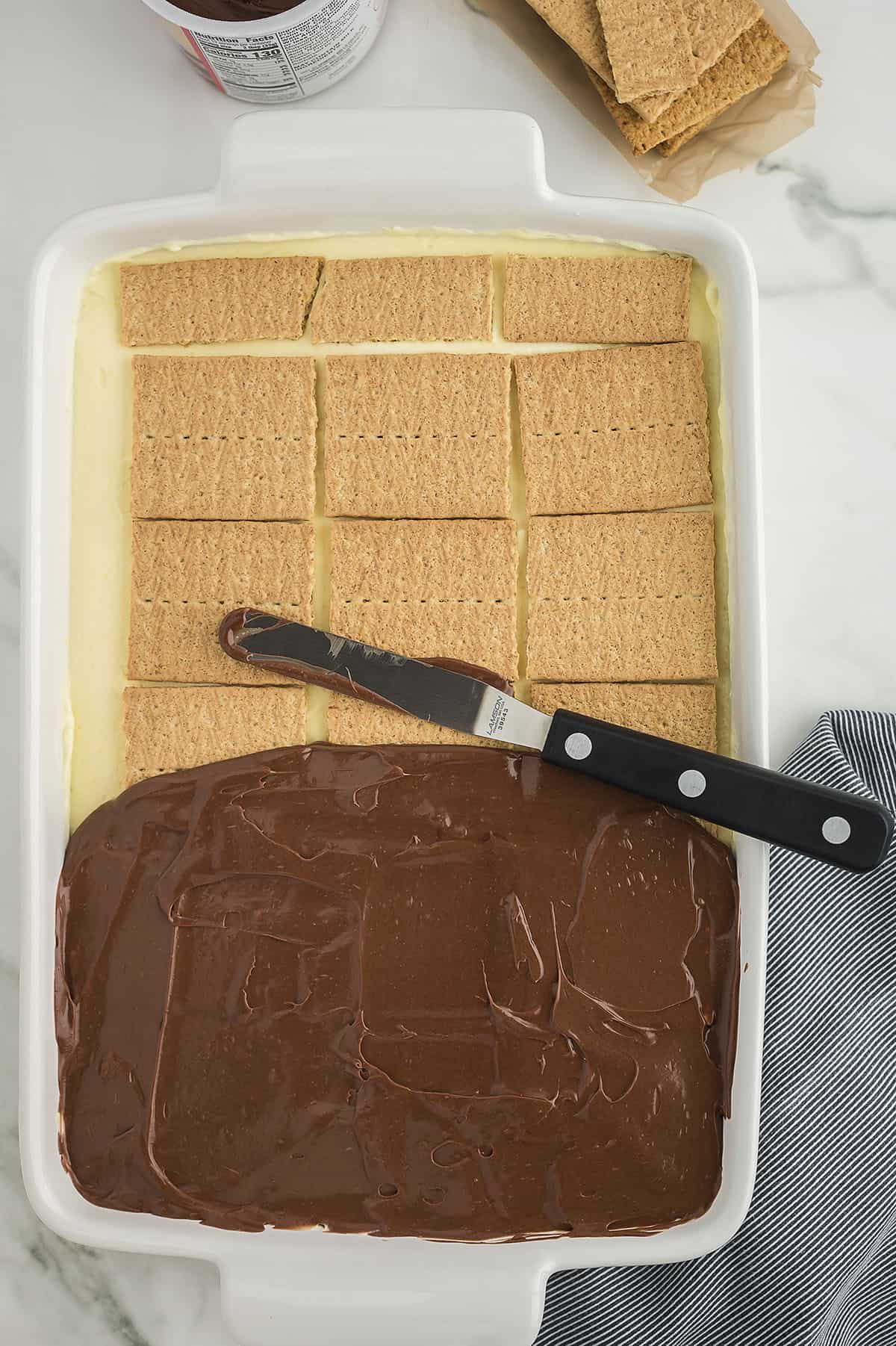 Chocolate frosting being spread over graham crackers.