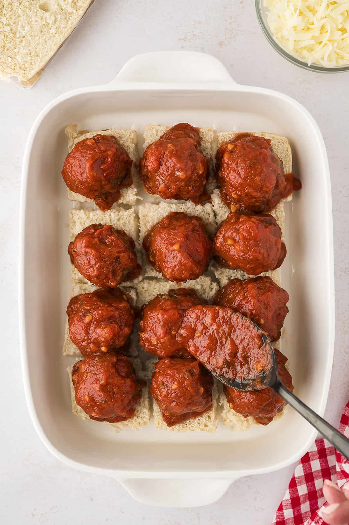 meatballs on slider rolls being topped with marinara.
