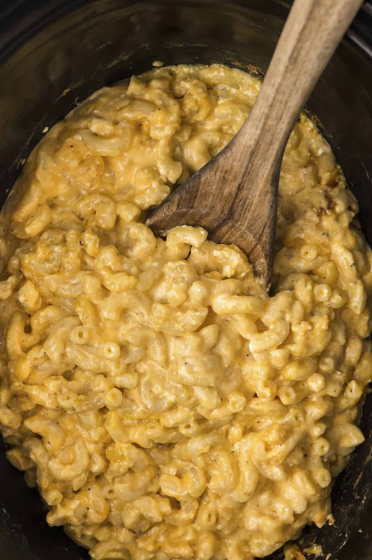 Crockpot mac and cheese with a wooden spoon.