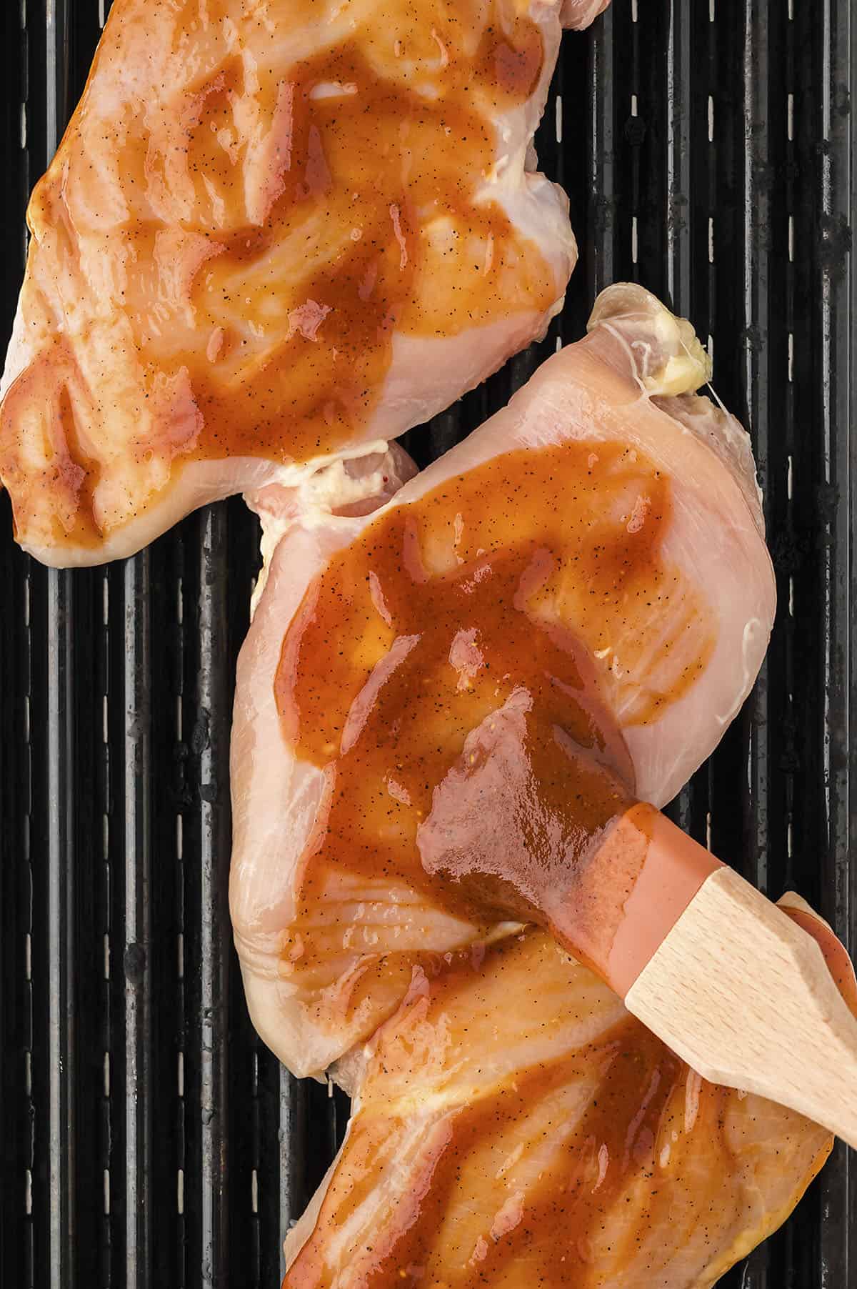 Barbecue sauce being brushed on chicken breasts on the grill.