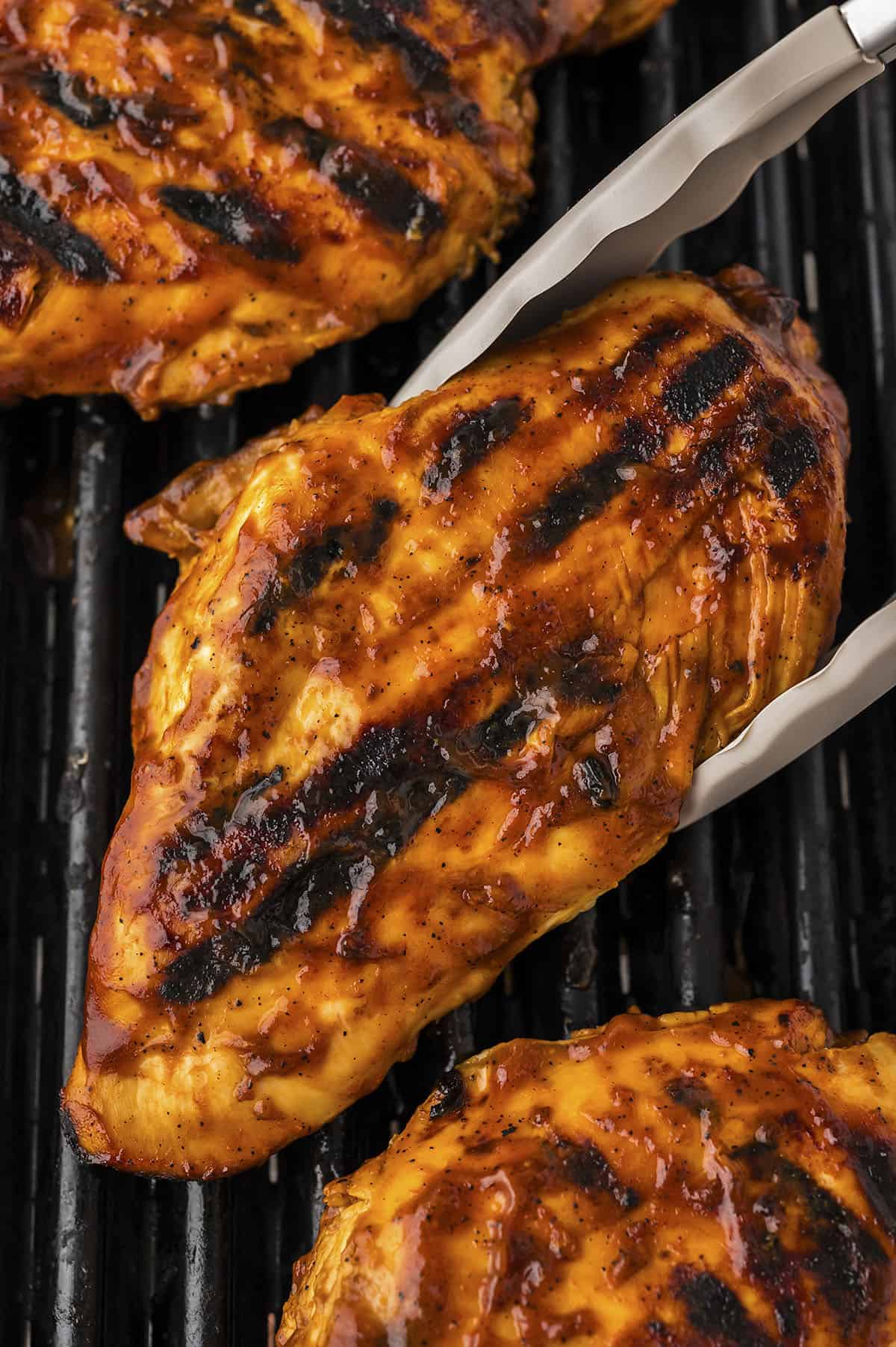 BBQ grilled chicken on the grill with tongs.