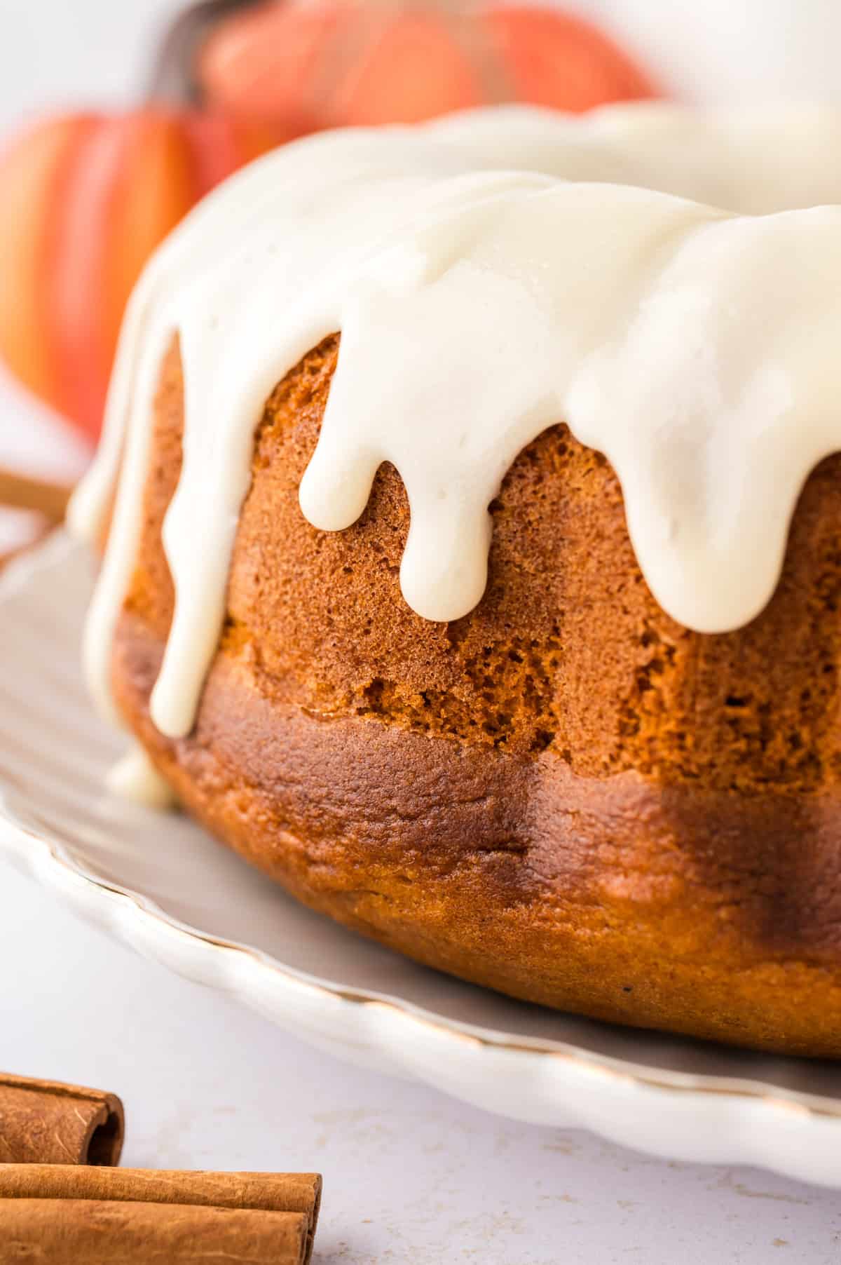 Pumpkin bundt cake topped with cream cheese glaze on cake plate.