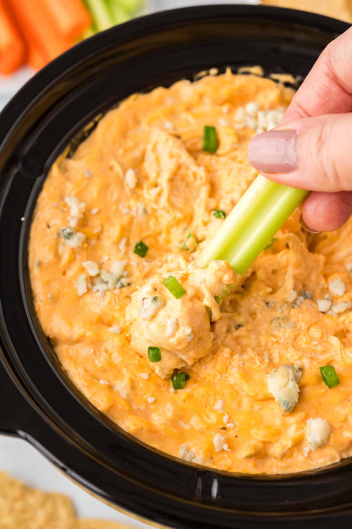 Celery being dipped into slow cooker buffalo chicken dip.