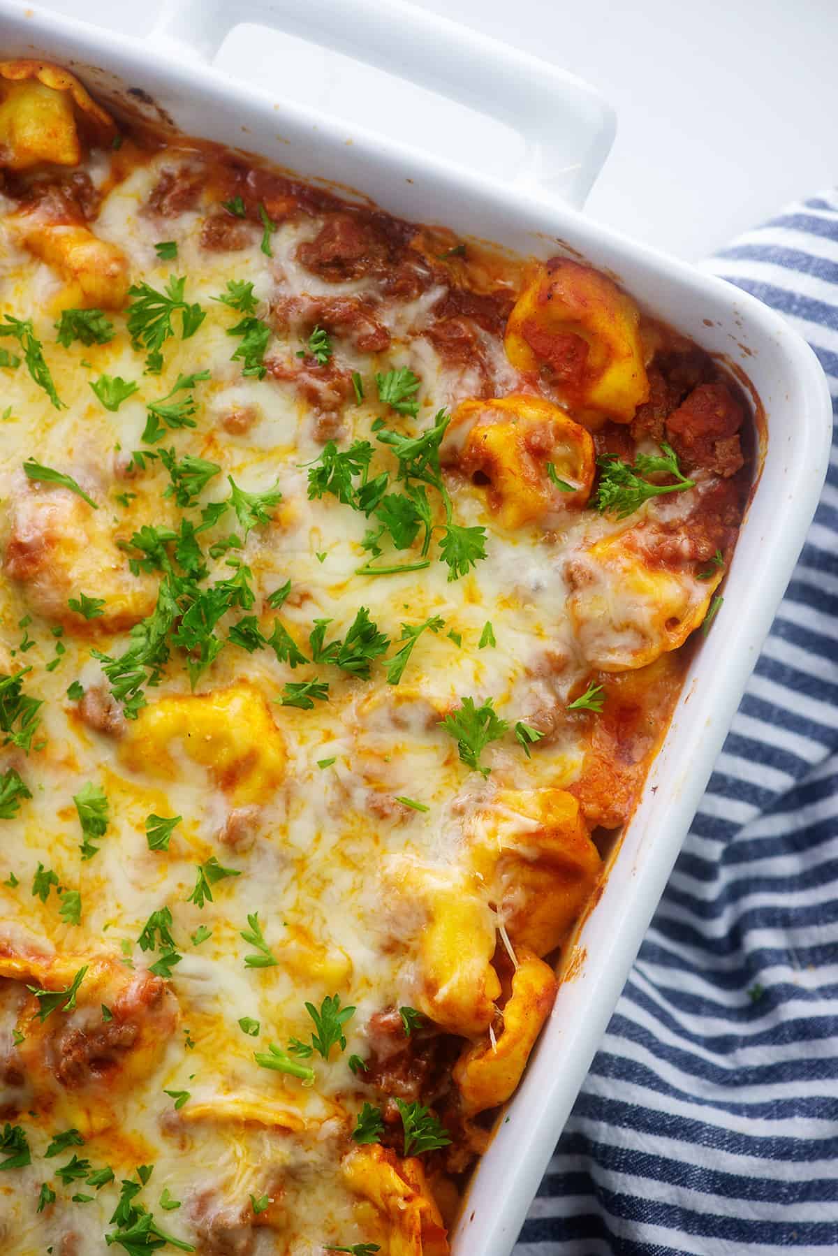 tortellini casserole in white baking dish topped with parsley.