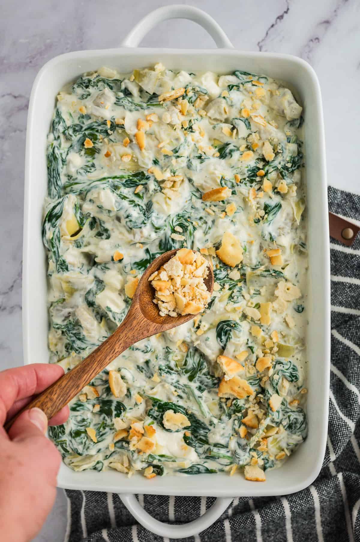 Crackers being sprinkled over spinach casserole in baking dish.