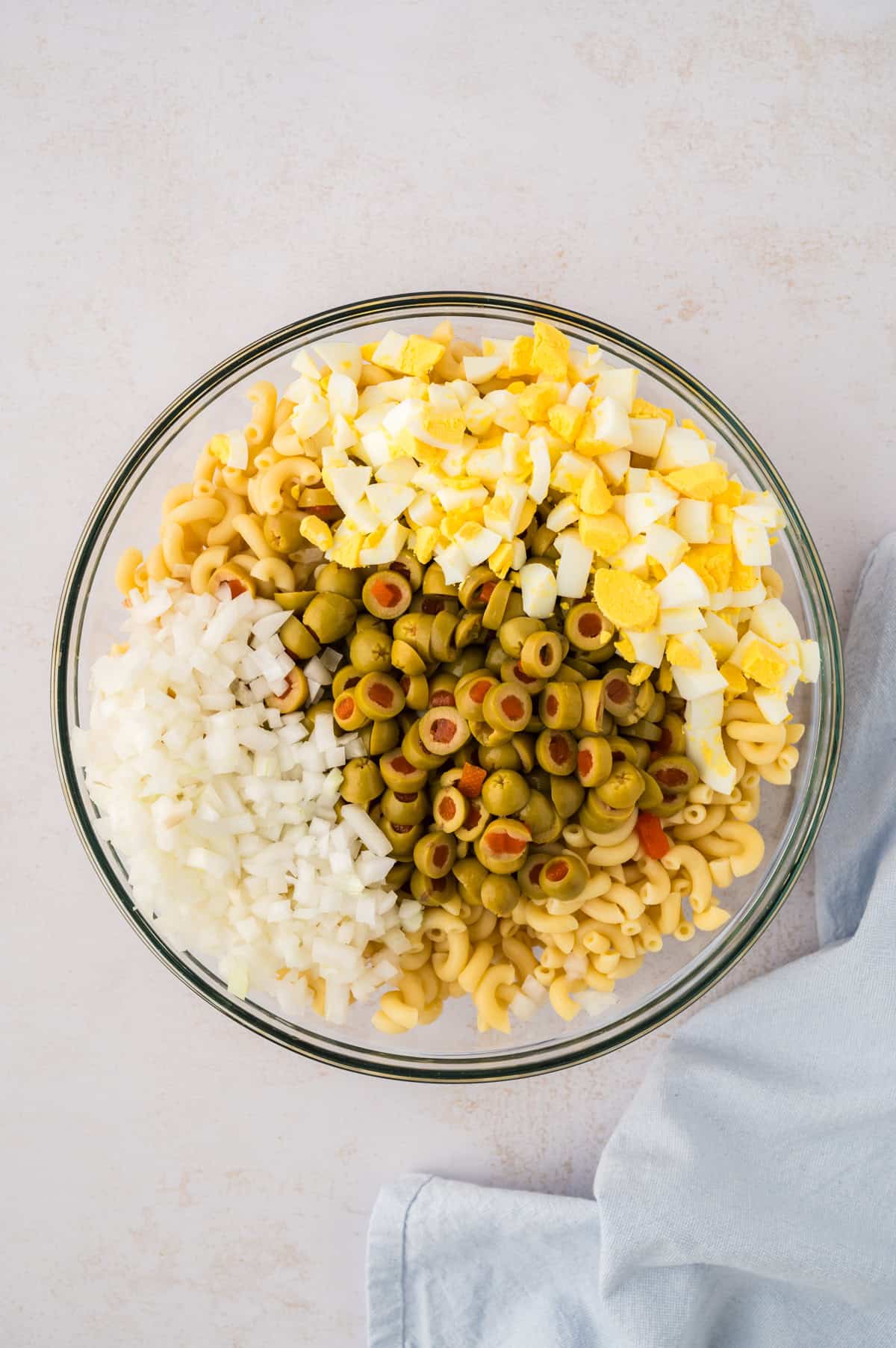 Cold macaroni with olives, onion, and eggs in a mixing bowl.