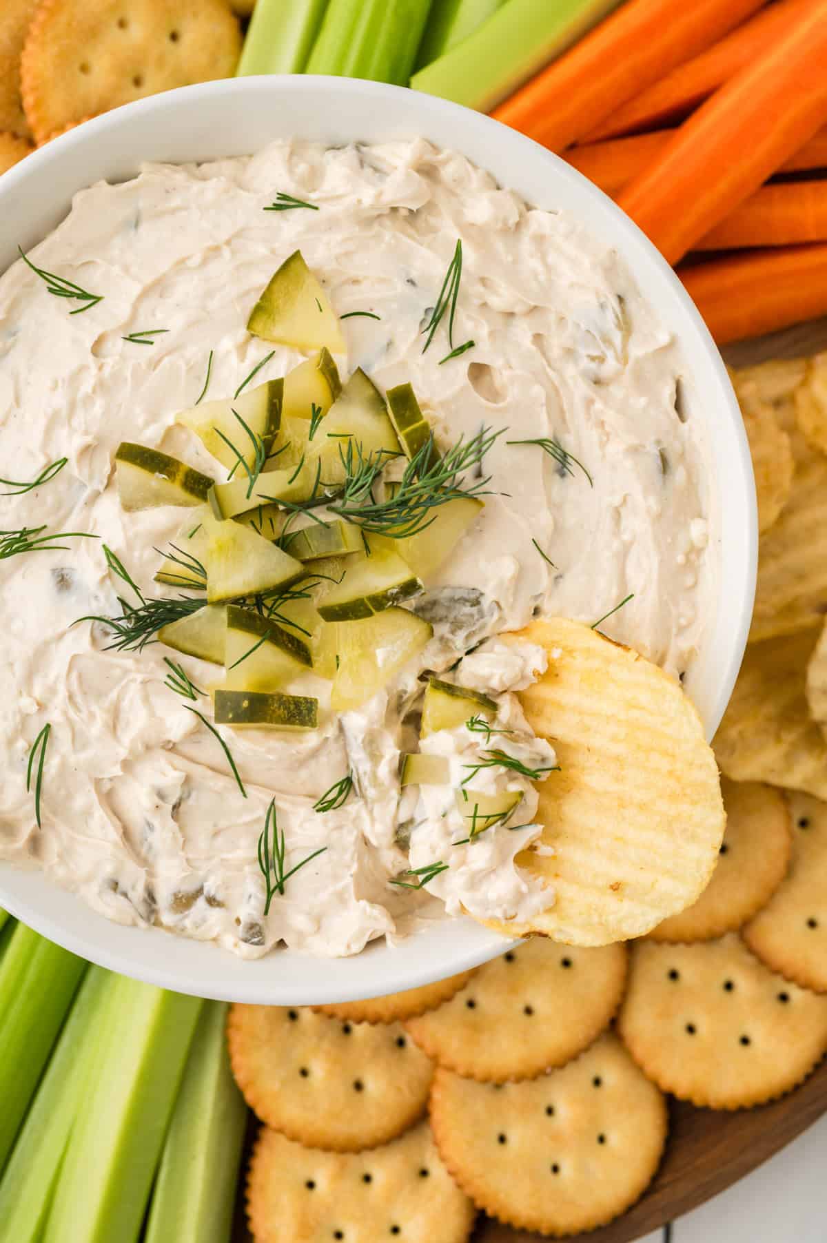 Dill pickle dip surrounded by crackers and vegetables.