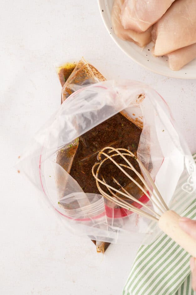 Person whisking together marinade ingredients in zip top bag.