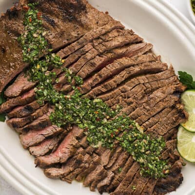 White platter filled with flank steak topped with chimichurri.