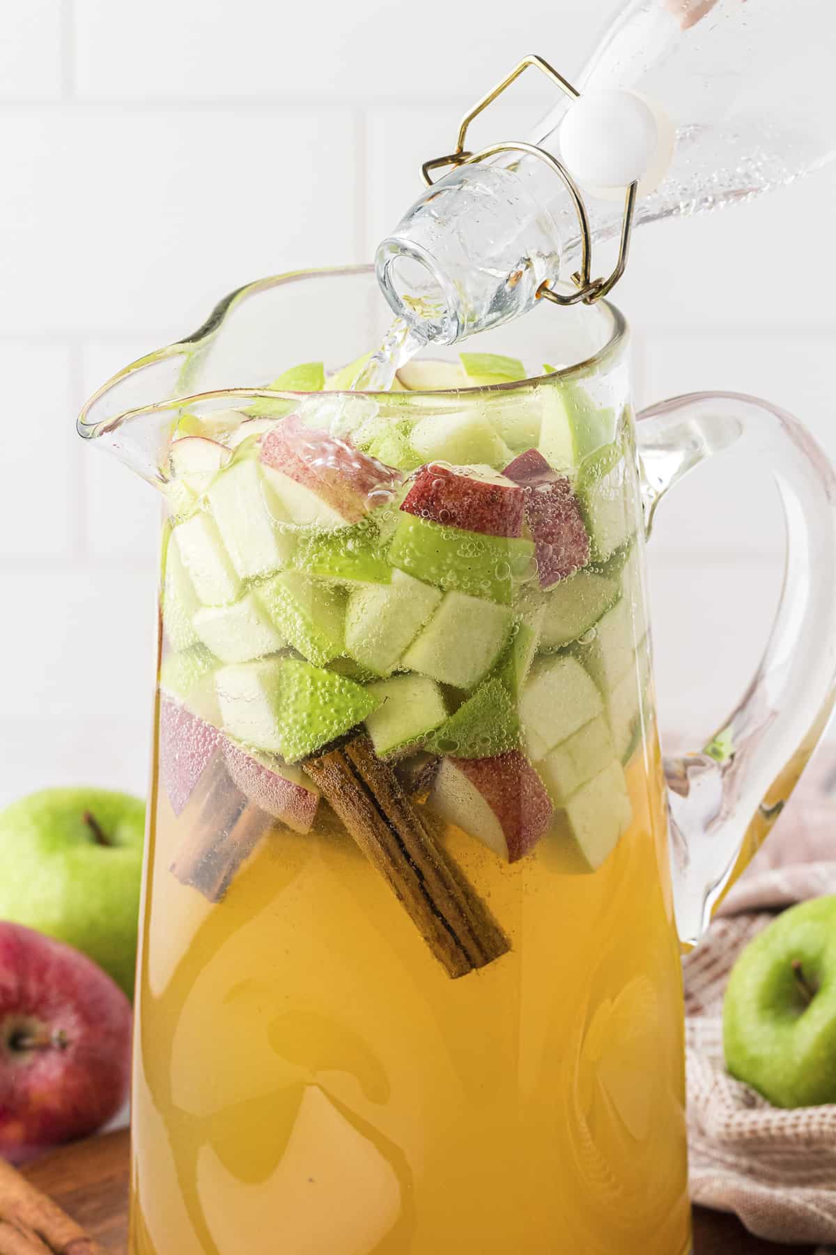 Bottle of club soda being poured into a pitcher of caramel apple sangria.