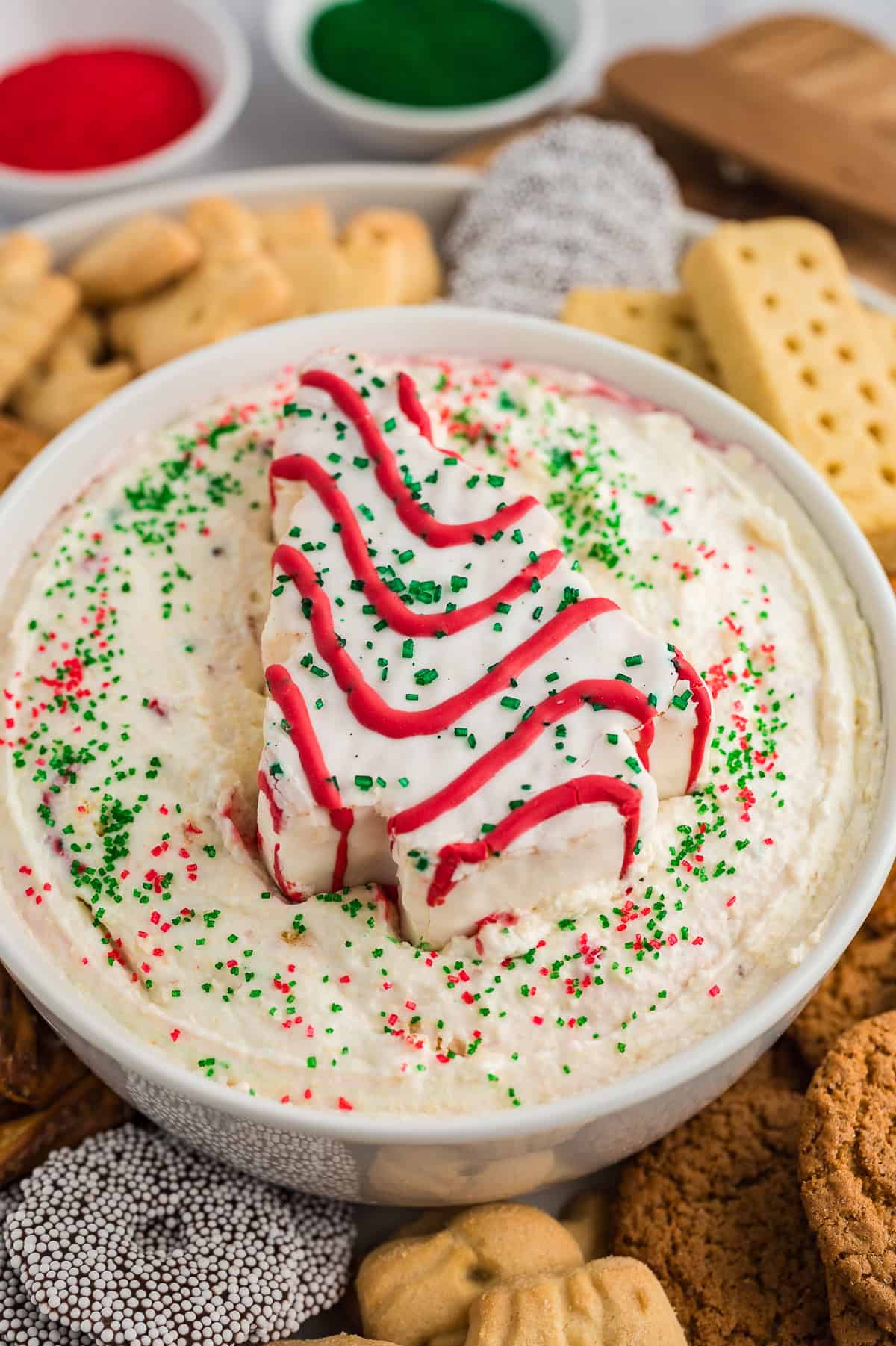 Christmas tree cake dip in white bowl surrounded by cookies.