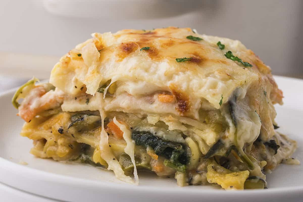 Slice of vegetable lasagna with white sauce on small white plate.