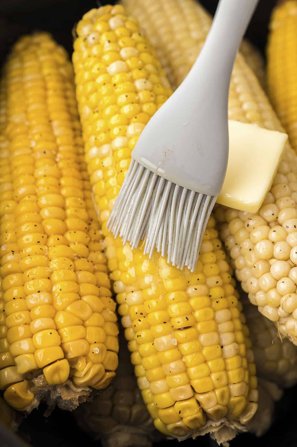 Corn being brushed with butter.