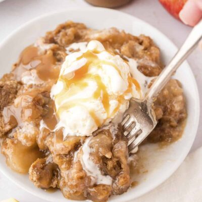 Fork taking a scoop of caramel apple dump cake from small white plate.